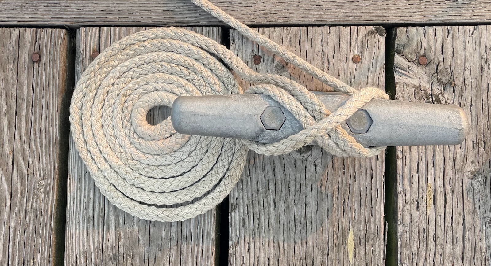 Mooring line coiled and belayed on a galvanised cleat on a weathered dock